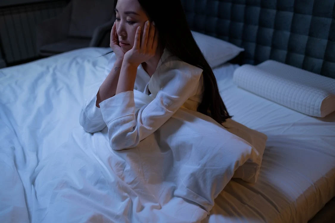 a woman sitting on a bed in a dark room struggling to sleep